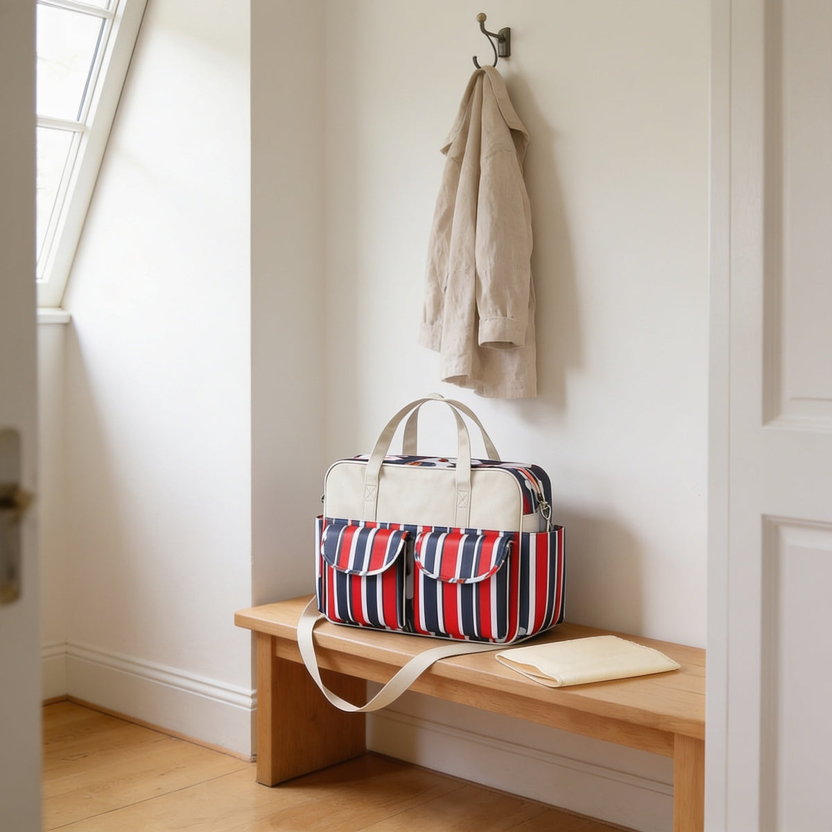 Red, navy and white stripe print diaper tote bag on a light oak hallway bench, its changing mat folded beside it.