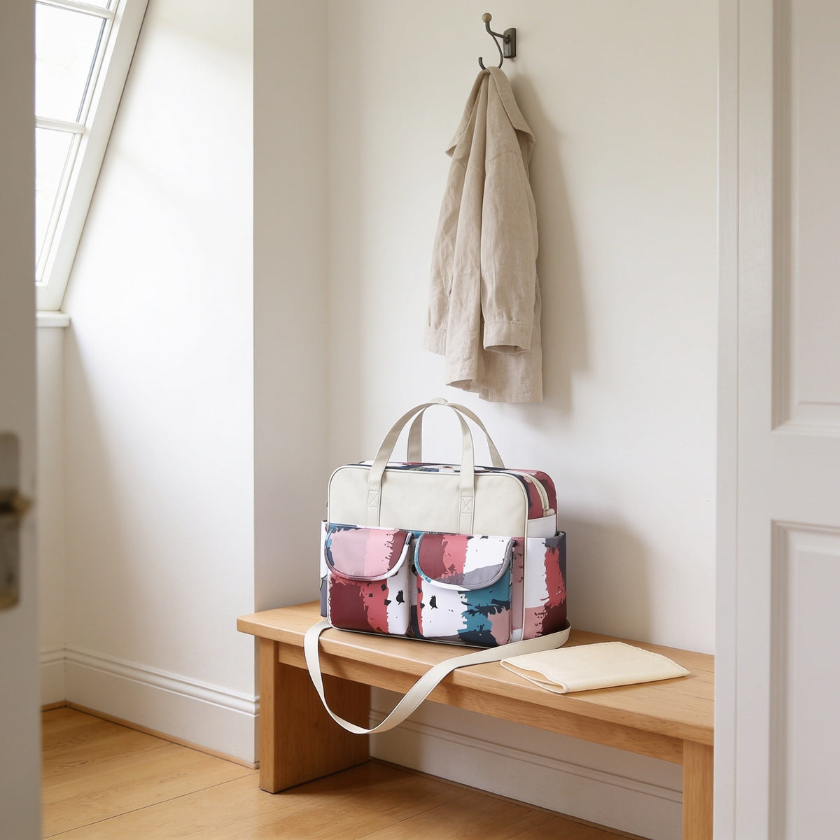 Pink, teal and burgundy color-block print diaper tote bag on a light oak hallway bench, its changing mat folded beside it.