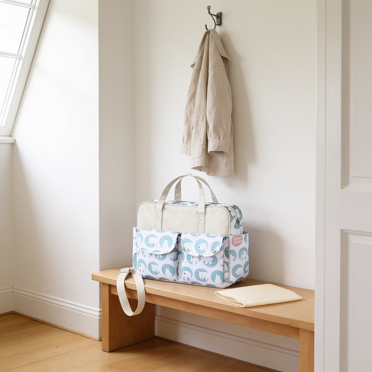 Polar bear print diaper tote bag on a light oak hallway bench, its changing mat folded beside it.