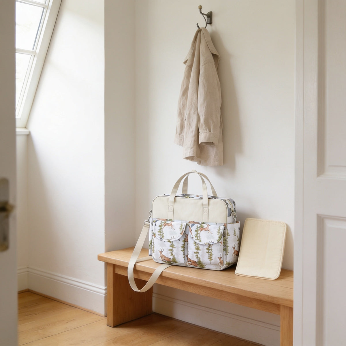 Woodland deer print diaper tote bag on a light oak hallway bench, its changing mat folded beside it.