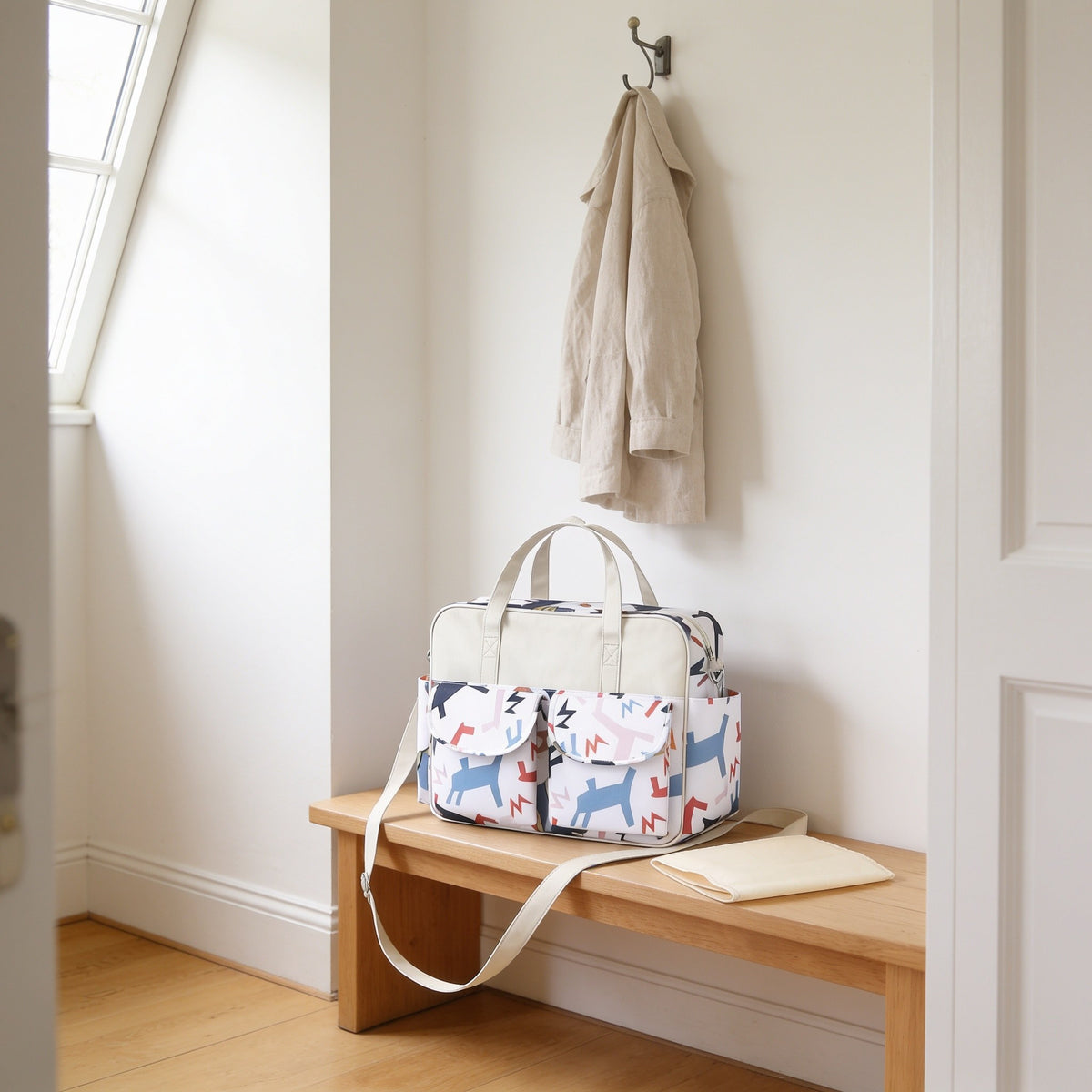 Colorful pony print diaper tote bag on a light oak hallway bench, its changing mat folded beside it.