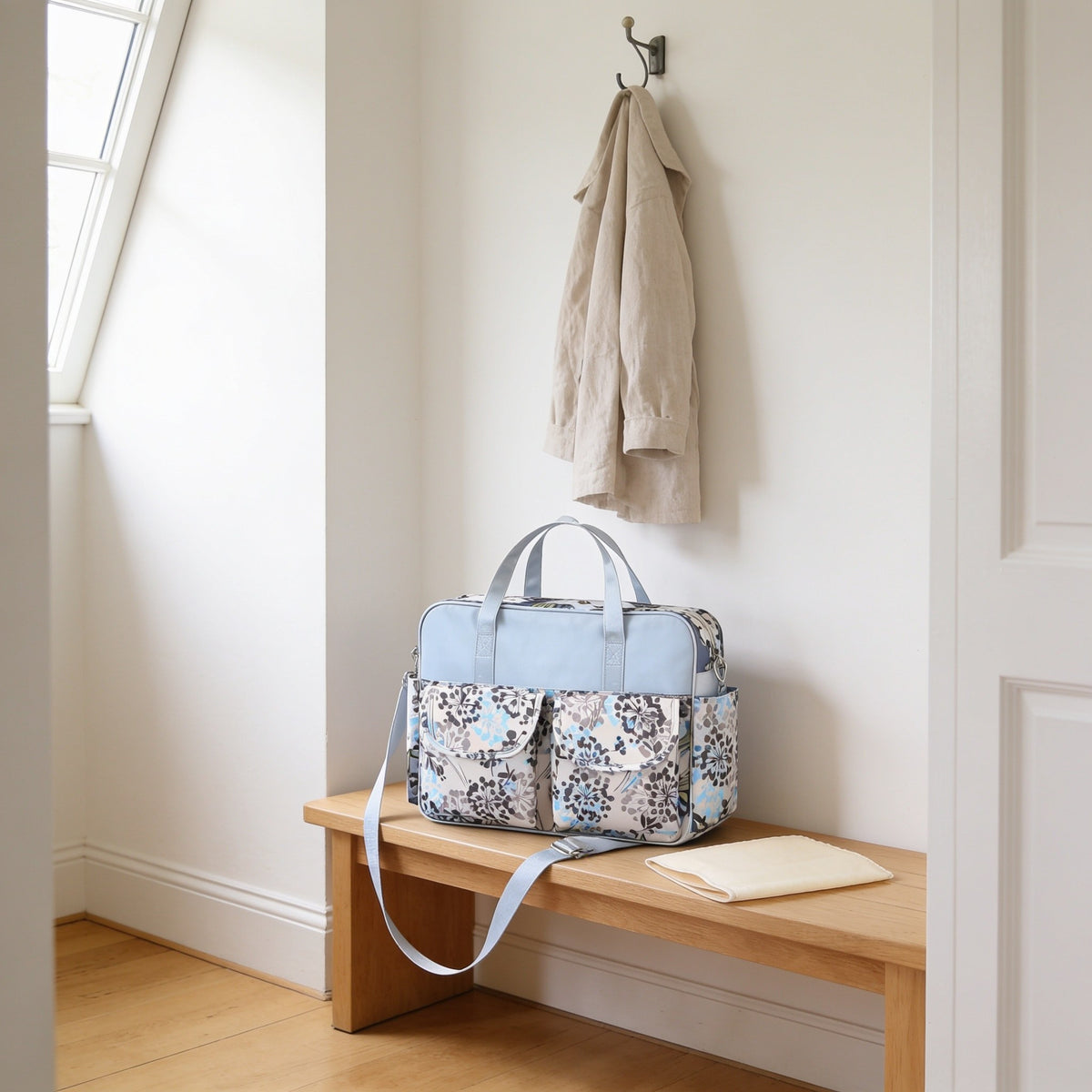 Dandelion print diaper tote bag on a light oak hallway bench, its changing mat folded beside it.