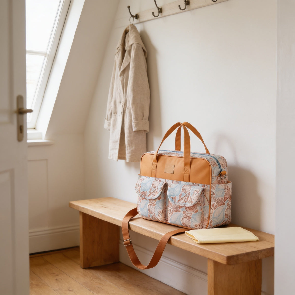 Seashell print diaper tote bag on a light oak hallway bench, its changing mat folded beside it.