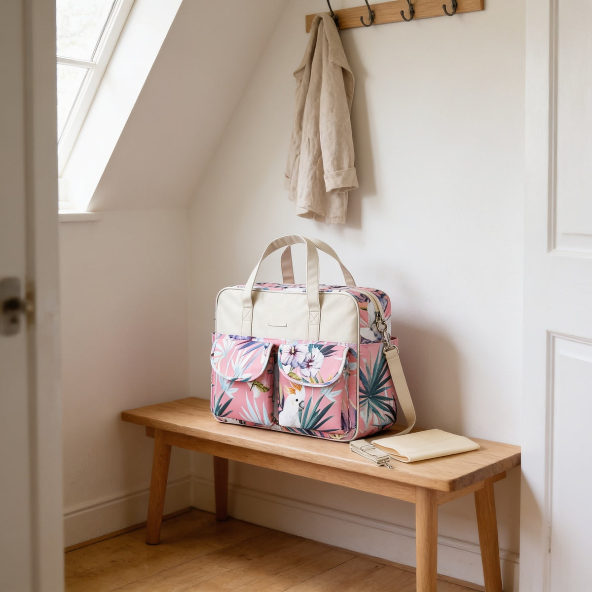 Pink tropical leaf print diaper tote bag on a light oak hallway bench, its changing mat folded beside it.