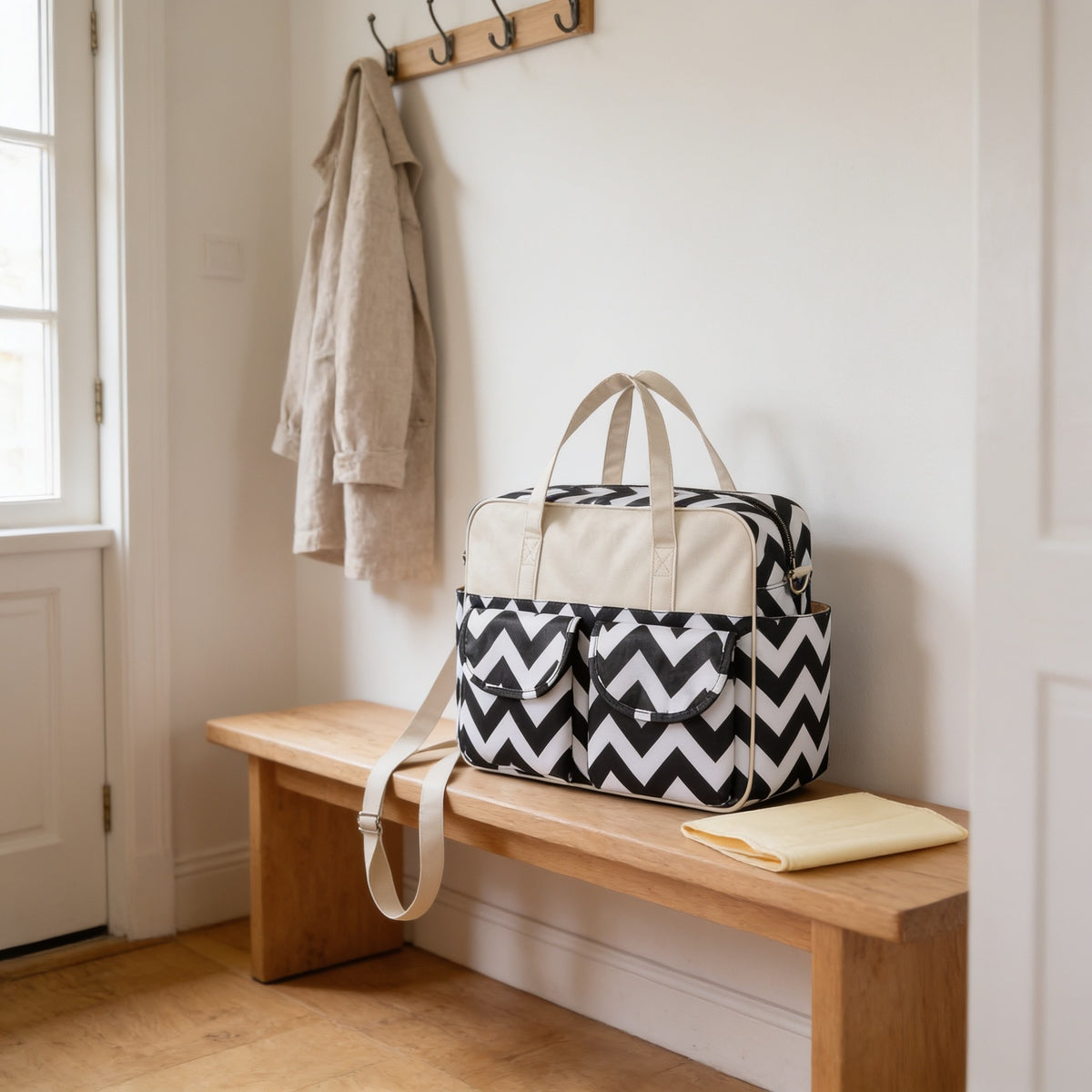 Black and white chevron print diaper tote bag on a light oak hallway bench, its changing mat folded beside it.