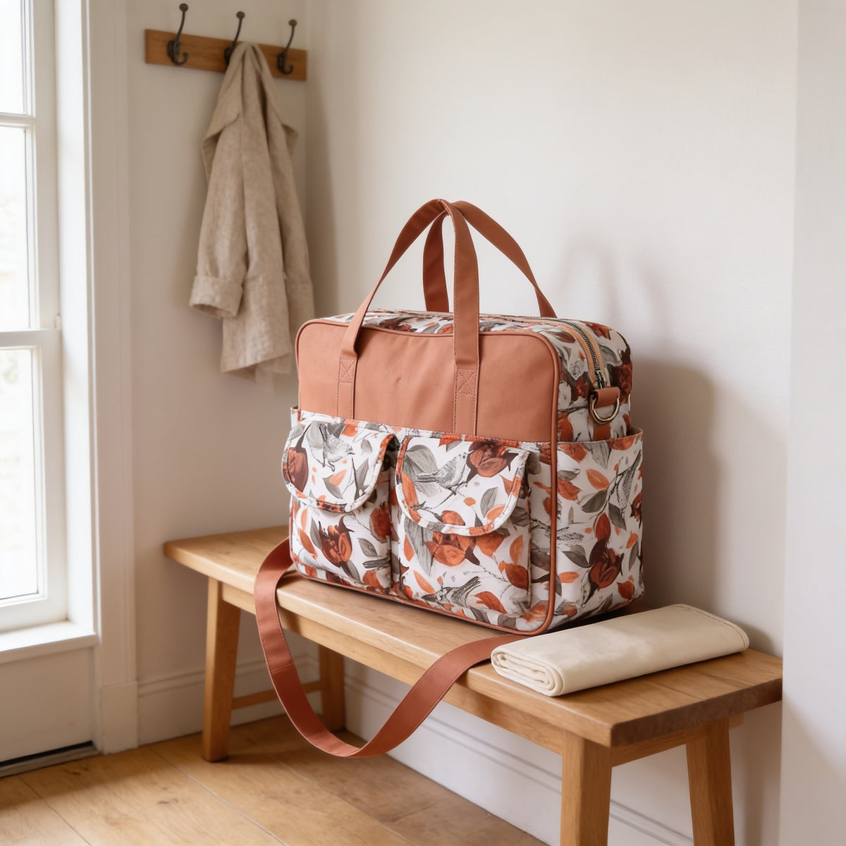 Rust floral print diaper tote bag on a light oak hallway bench, its changing mat folded beside it.