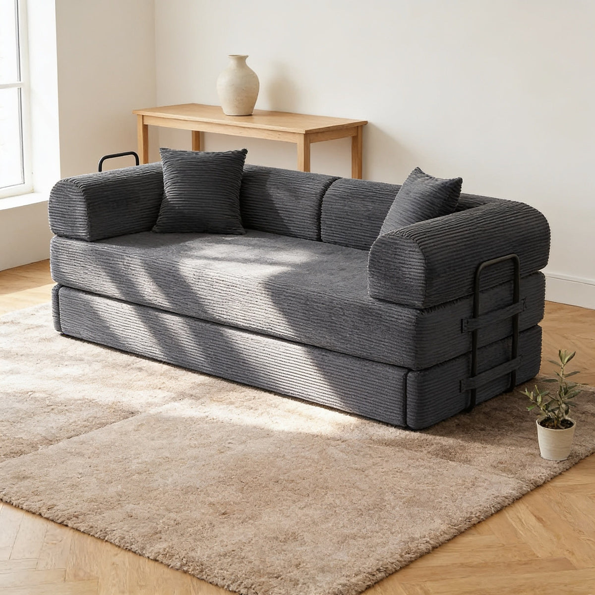 Dark charcoal grey corduroy convertible sofa bed in sofa mode in a warm living room.
