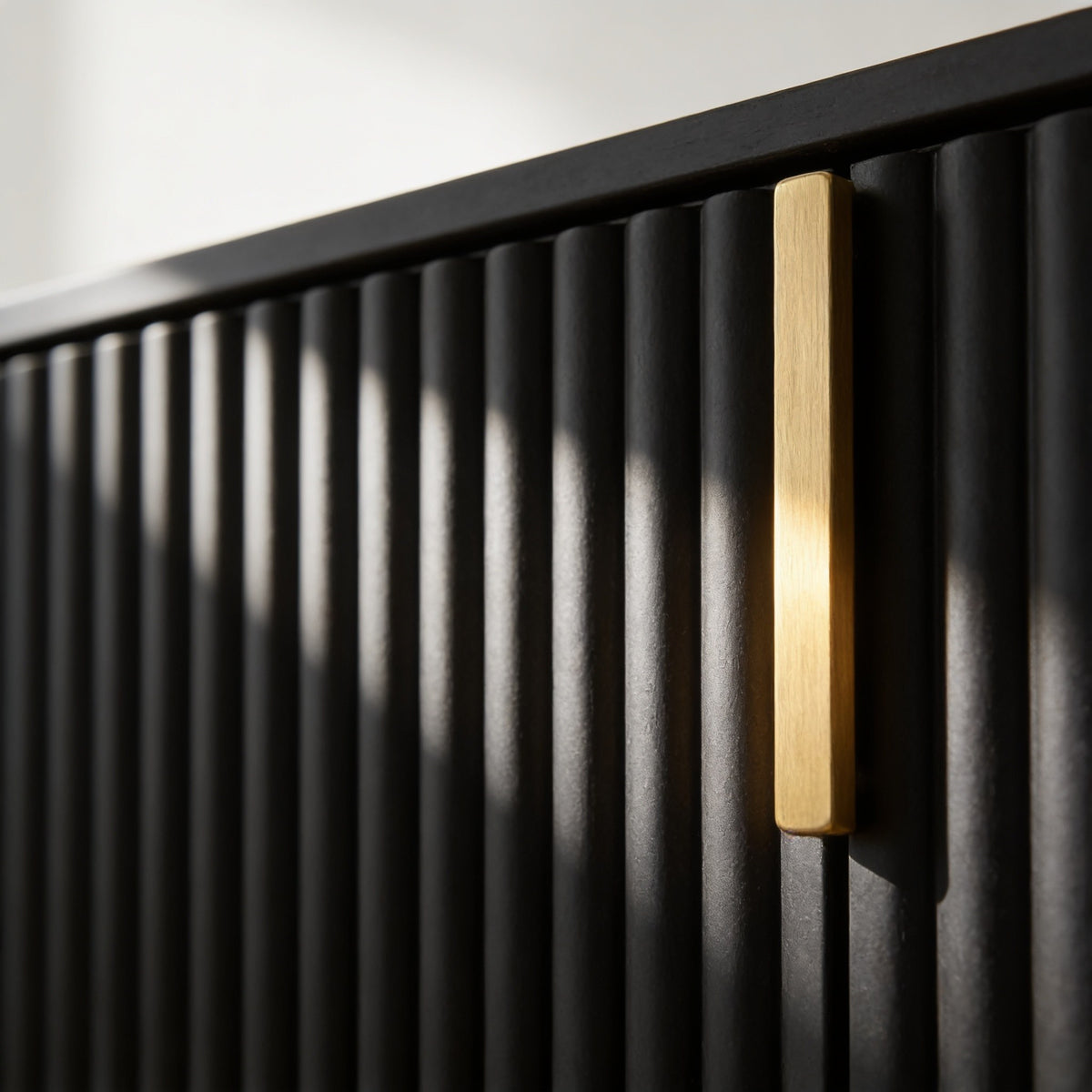 Macro detail of the cabinet's matte black fluted door ribs beside its slim brushed gold bar handle.