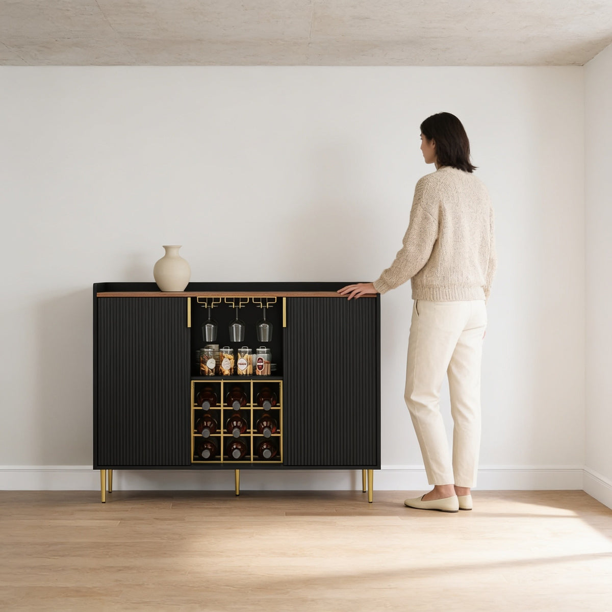 Adult standing beside the fluted coffee bar cabinet, whose walnut top reaches her hip at ninety-four and a half centimetres.